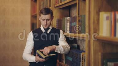 男记者在书架附近为文章阅读书籍制作研究。 聪明的作家拿着书分析